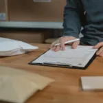 Seseorang mengisi formulir pemesanan barang di clipboard dengan paket di sekitarnya